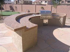 an outdoor bbq and grill area in a backyard with stone pavers around it