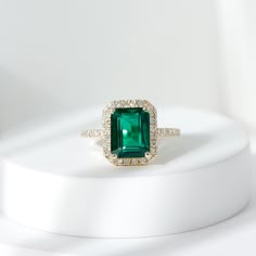 an emerald and diamond ring sitting on top of a white surface with diamonds around it