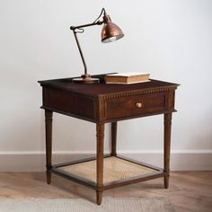 an antique desk with a lamp on top and a book under the table next to it