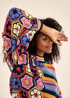 a woman in a colorful sweater covering her face with her hands and looking at the camera