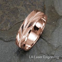 a rose gold wedding ring with an arrow in the center on a stone background that says la laser engraving