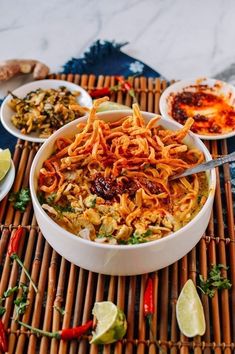 a bowl filled with noodles and vegetables on top of a bamboo mat next to bowls of sauce