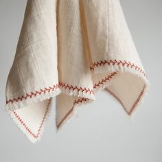 two white towels hanging from a hook with red stitching on them and one is folded over the other