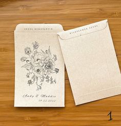 two envelopes with flowers on them sitting on a wooden table