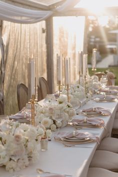 a long table is set with white flowers and candles for an elegant wedding reception at sunset