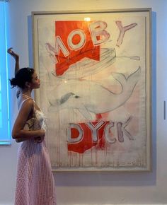 a woman standing in front of a painting with words on it and an image behind her