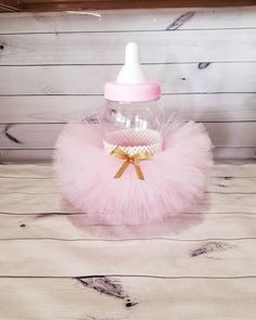 a baby bottle with a pink tutule and gold bow on the top sitting on a wooden table