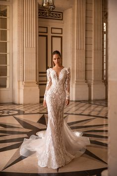 a woman in a white wedding dress standing on a marble floor with columns and chandelier