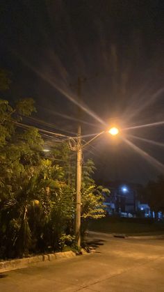 an empty street at night with the lights turned on and trees in the foreground