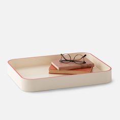 a pair of glasses sitting on top of a book in a white tray with red trim