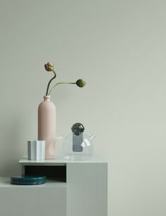 a white table with a pink vase and other items on it in front of a gray wall