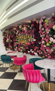 pink and green chairs sit in front of a floral wall at shera, which is decorated with flowers