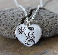 "This necklace features a handmade fine silver (99.9% pure silver) heart pendant stamped with a sweet little Totoro with a flower and a friendly soot sprite. The stamping is oxidized to make it stand out and the rest of the pendant is matte silver. The heart charm is about 7/8\" wide and 3/5\" tall (22x18mm) and is hung on a delicate sterling silver chain finished off with a sterling silver lobster clasp. I have a few other Totoro themed items in my shop. See them here: https://www.etsy.com/shop Cute Silver Sterling Silver Charm Necklaces, Cute Nickel-free Sterling Silver Necklaces, Cute Sterling Silver Pendant Charm Necklace, Cute Sterling Silver Pendant Charm Necklaces, Cute Silver Charm Necklace With Heart Charm, Cute Sterling Silver Necklace Gift, Handmade Small Sterling Silver Charm Necklaces, Cute Sterling Silver Necklace For Gift, Handmade Unique Sterling Silver Charm Necklaces