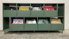 a green bookcase filled with lots of books on top of cement floored floors