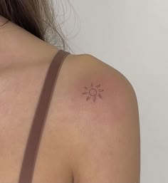 the back of a woman's shoulder with a small sun tattoo on it