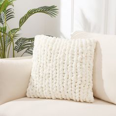 a white pillow sitting on top of a couch next to a potted palm tree