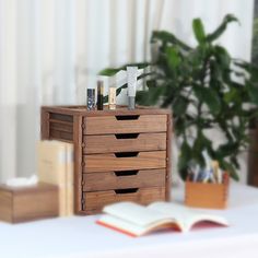 an open book is sitting on a desk next to a wooden drawer with three drawers