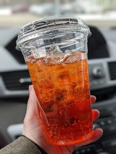 a person holding up a plastic cup filled with ice and soda in their hand while driving