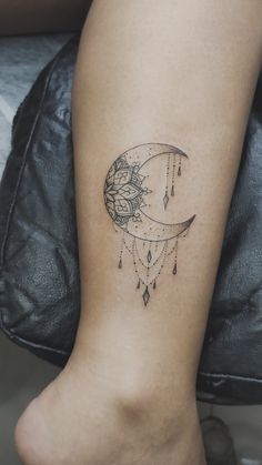 a woman's leg with a tattoo on it that has a crescent moon and flowers hanging from it