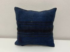 a dark blue pillow sitting on top of a white table next to a gray wall