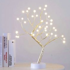 a small tree with white lights on top of a table next to some books and a book