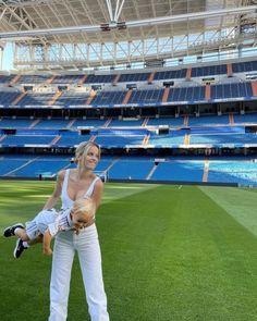 a woman holding a baby in her arms at a baseball game with the stands empty