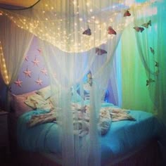 a canopy bed with white curtains and fairy lights on the headboard is decorated in pastel colors