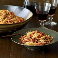 a plate of spaghetti with tomato sauce next to a bowl of wine and two glasses