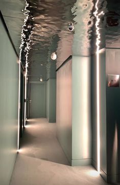 an empty hallway with lights on the ceiling and water reflecting off the walls in front of it