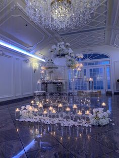 a large centerpiece with candles and flowers on the floor in front of a chandelier