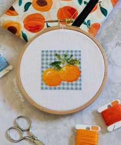 an orange cross - stitch pattern with scissors, thread and spools on a marble surface