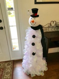 a snowman made out of white feathers in front of a door with a black top hat