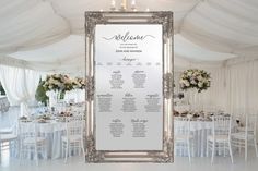 a white and silver wedding seating plan on a large framed mirror in the middle of a room