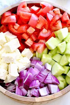 a wooden bowl filled with chopped vegetables and diced cheese on top of each other