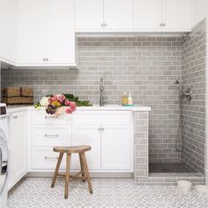 an image of a kitchen with white cabinets and grey tile on the walls, along with a small stool