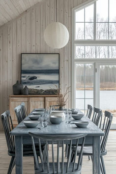 a dining table with chairs and plates on it in front of a large window that looks out onto the water