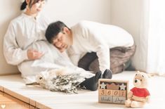 a man and woman are laying on the floor next to a teddy bear with a calendar