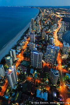 an aerial view of a city at night with the ocean in the foreground and lights on