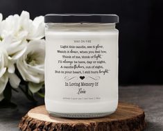 a white candle with a poem on it next to some flowers and a wooden slice