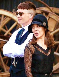 a man and woman standing next to each other in front of an old wooden structure