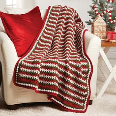 a white chair with a red and green blanket on it next to a christmas tree