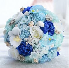 a bridal bouquet with blue flowers and seashells on the bottom is sitting on a table