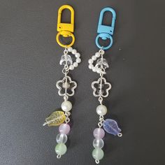 two pairs of earrings with charms attached to them on a black surface, one is yellow and the other is blue