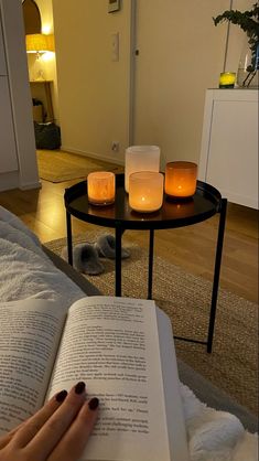 a person is reading a book with candles on the table in front of them,