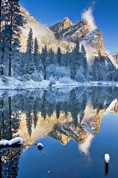 the mountains are covered in snow and there is a lake surrounded by pine trees with fog