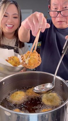 a man and woman are cooking food in a large pot on the stove with tongs