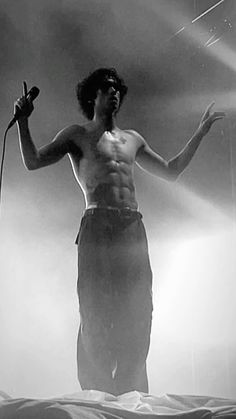 a man standing on top of a bed with his hands in the air while holding a microphone