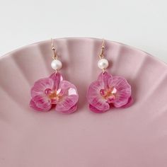 These stunning handmade earrings feature delicate pink orchid flowers made from shrink plastic, suspended from a hook-style earring finding. The flowers are beautifully adorned with freshwater pearls, adding a touch of elegance and sophistication to the design. The shrink plastic material used to make the flowers is lightweight and durable, making these earrings perfect for everyday wear. The intricate design of the orchid petals is truly eye-catching and sure to be a conversation starter. These Cute Earrings Handmade, Orchid Clothes, Shrink Plastic Earrings, Shrink Plastic Jewelry, Pink Pearl Earrings, Orchid Earrings, Plastic Earrings, Orchid Flowers, Pink Orchids