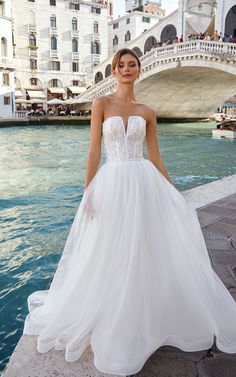 a woman in a white wedding dress standing by the water