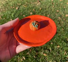 a hand holding an orange frisbee in the grass